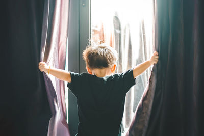 Rear view of man with arms outstretched standing against window