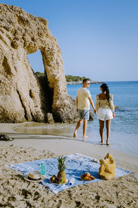 People standing on rock by sea against clear sky