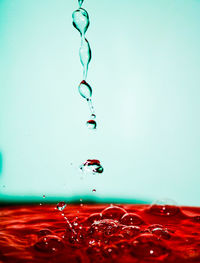 Close-up of drop falling on red water against blue background