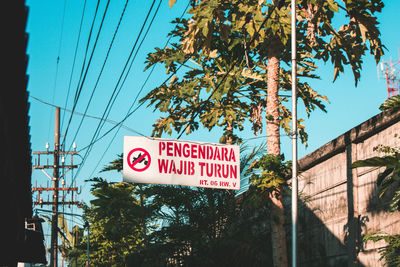 Low angle view of road sign by trees against blue sky