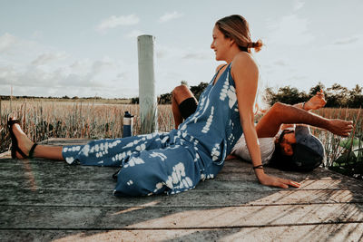 Side view of young woman sitting against sky