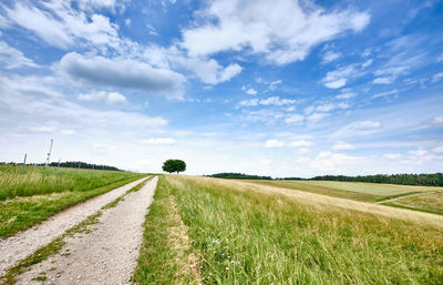 Dirt road amidst field against sky