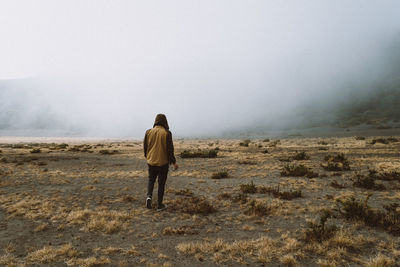 Rear view of man standing on field in foggy weather