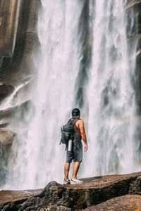 Man standing on rock looking at waterfall