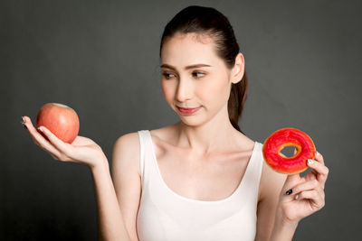 Woman holding apple and donut against gray background