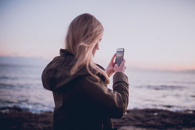 Young woman photographing while standing on beach