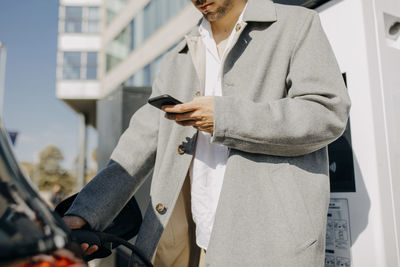 Man using smart phone charging electric at station