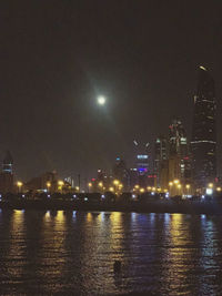 Illuminated city by river against sky at night