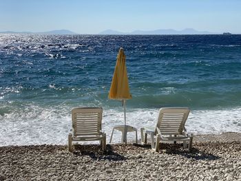 Empty chairs on beach against sky