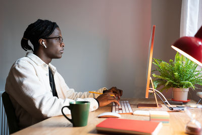 Focused african man freelance web developer writing code, using computer, sitting at home office