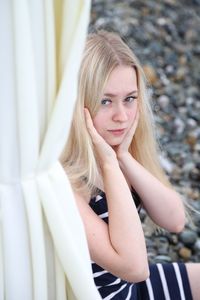 Teenage girl with blond hair sitting by curtain