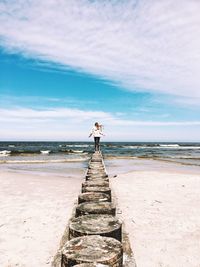 Rear view of girl standing on wood at beach against sky