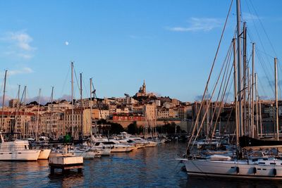 Sailboats moored at harbor in city against sky