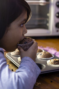 An indian girl child eating a homemade chocolate muffin cup cake baking tray with selective focus