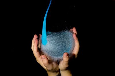 Close-up of hand holding blue glass against black background