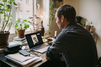 Businessman with coffee cup discussing with colleague on video call at home office