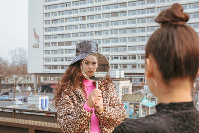 Woman showing mirror to friend in city