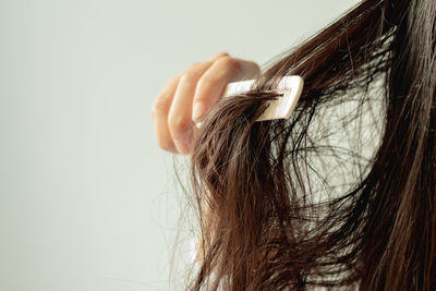 Close-up of woman combing hair against white background