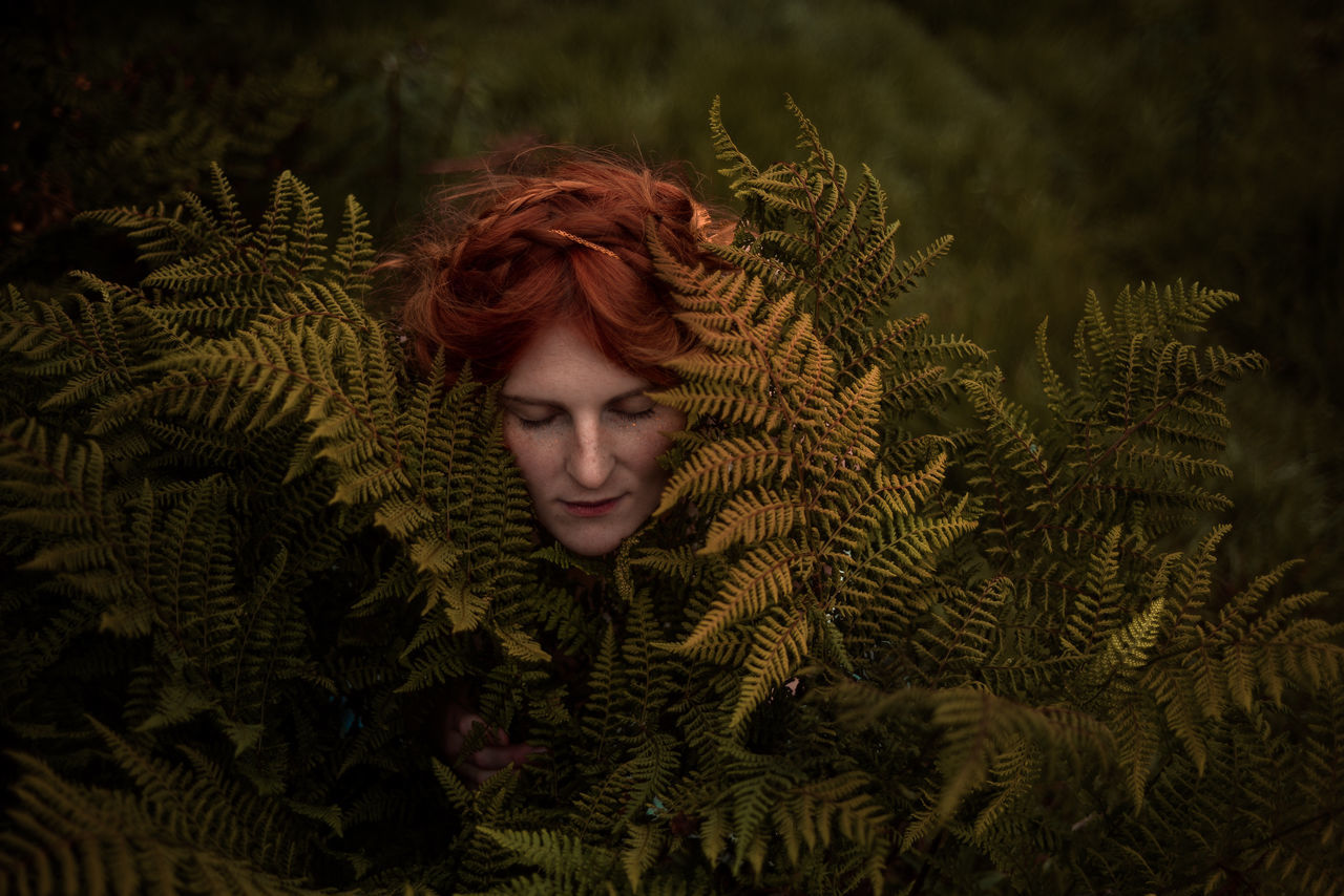 one person, real people, young adult, front view, young women, leisure activity, lifestyles, redhead, portrait, plant, adult, eyes closed, nature, green color, headshot, hairstyle, growth, leaf, contemplation, beautiful woman, warm clothing, pine tree