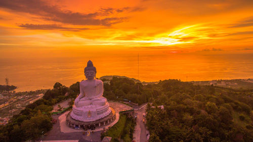 Statue by temple against sky during sunset