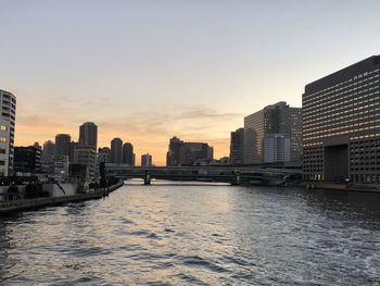 River amidst buildings in city against sky during sunset