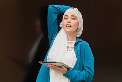 Portrait of young woman holding digital table against black background