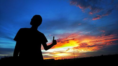 Low angle view of silhouette man showing thumbs up while standing against sky during sunset