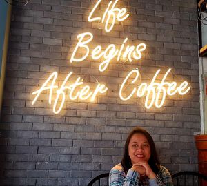 Smiling woman sitting against illuminated text on wall at cafe