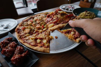 Midsection of person holding pizza in plate on table