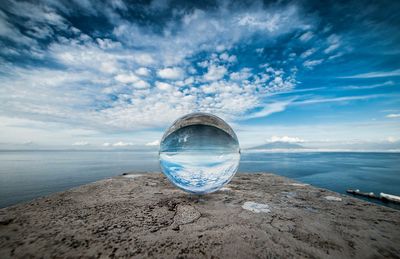 Close-up of crystal ball on beach against sky