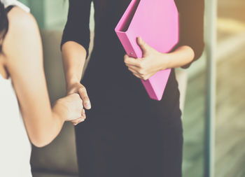 Midsection of female colleagues giving handshake while standing in office