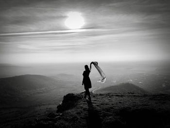 Monchrome photo of woman standing on top of the mountain holding a scarf floating in the wind
