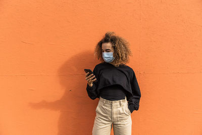 Portrait of young woman standing against orange wall