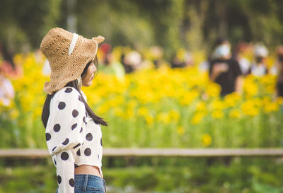 Rear view of woman standing against yellow flowering plants