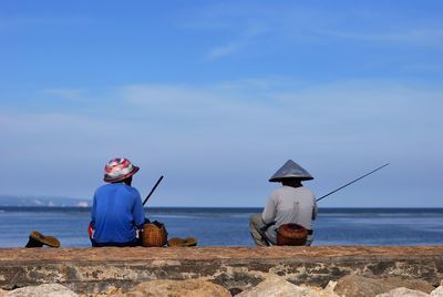 Rear view of men fishing by lake against sky