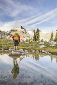 Rear view and reflection of backpacker looking at mountain summit.