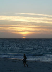 Silhouette woman on beach against sky during sunset