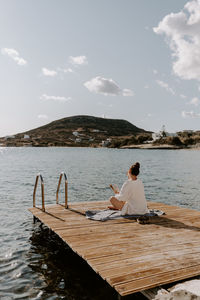 Rear view of woman sitting on pier by sea