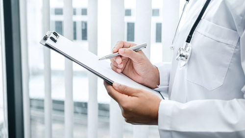 Midsection of doctor writing on clipboard