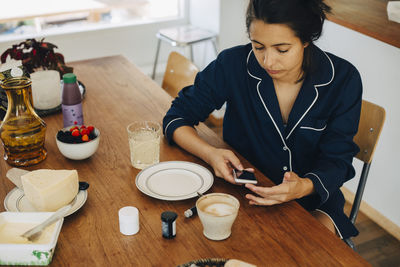 Woman checking blood sugar level while having breakfast on table at home