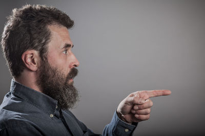 Side view of bearded man pointing against gray background