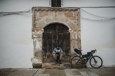 Cyclist with bicycle sitting in front of old door