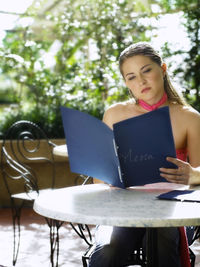 Mid adult woman reading menu while sitting on table at restaurant