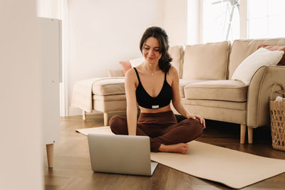 Fitness girl looks at her laptop while doing sports training and physical activity at home