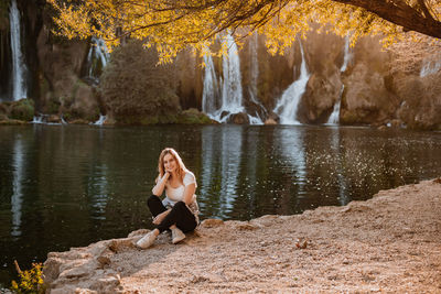 Young woman sitting on rock by lake