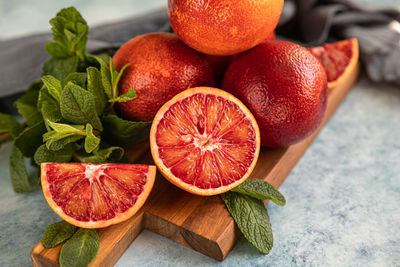 Whole and cut in half blood sicilian oranges, limes and mint on blue concrete background.