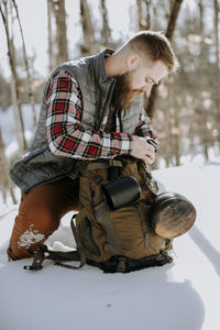 Man with bead wearing flannel and vest kneels in snow with pack