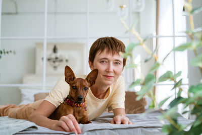 Mature woman lies on floor with slittle dog miniature pinscher