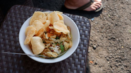 A white bowl of chicken porridge on a plastic chair at a street food vendor