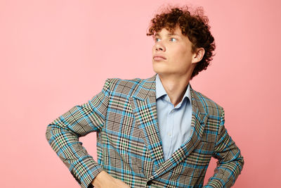 Young man standing against pink background